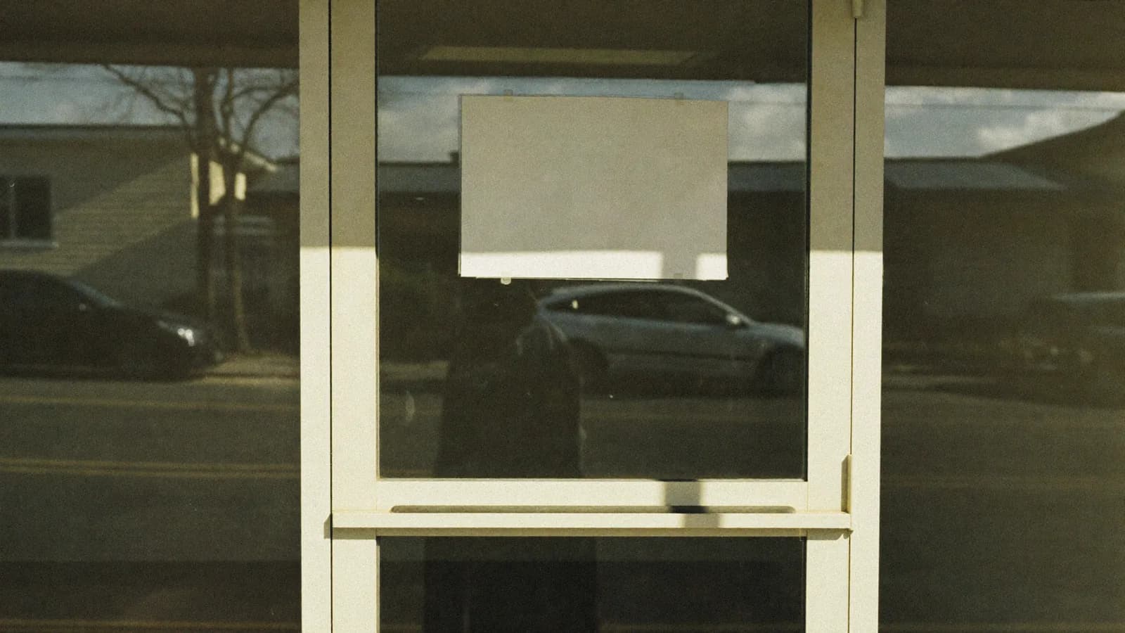 La puerta de cristal de un local cerrado, con un cartel en blanco pegado por dentro.